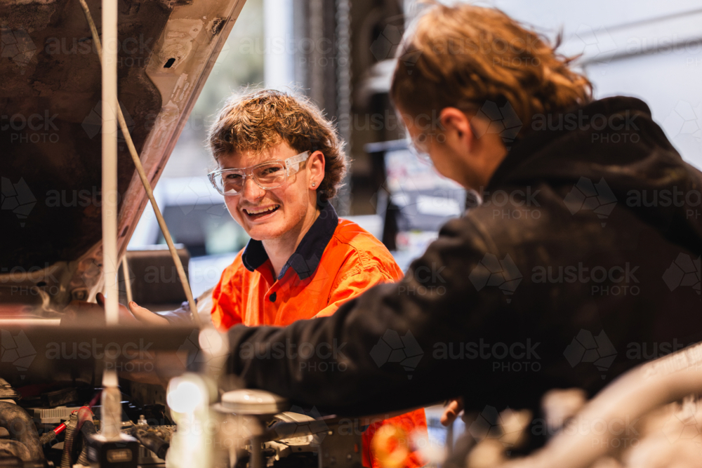 portrait of smiling man in workwear working on car vehicle engine in mechanics workshop - Australian Stock Image