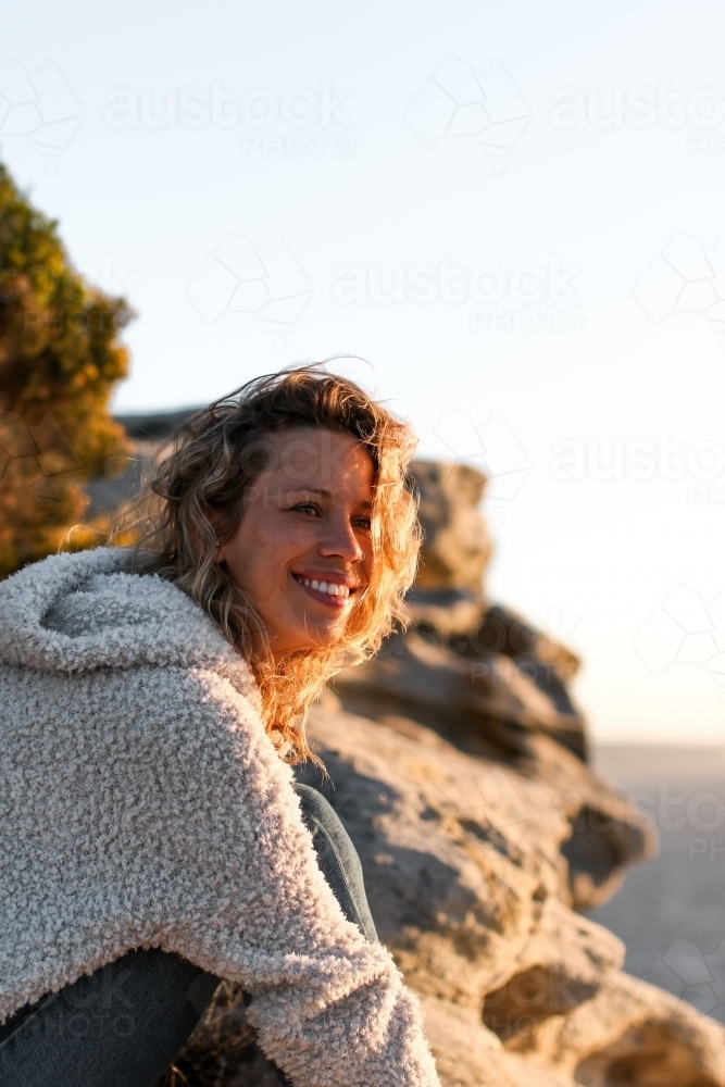Portrait of smiling young woman on coastal clifftop at sunrise - Australian Stock Image