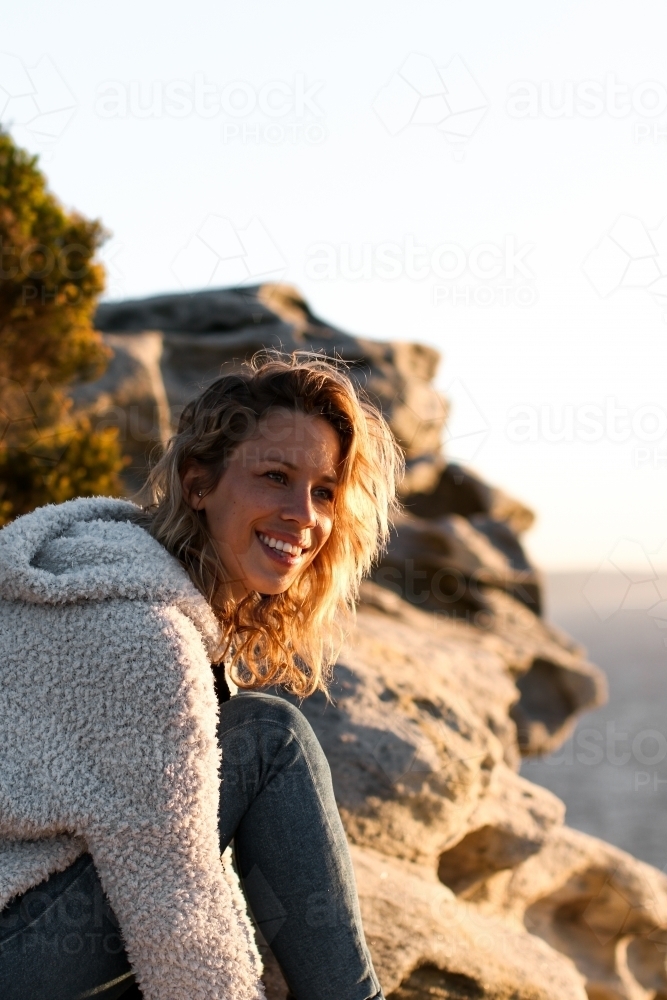 Portrait of smiling young woman on coastal clifftop at sunrise - Australian Stock Image