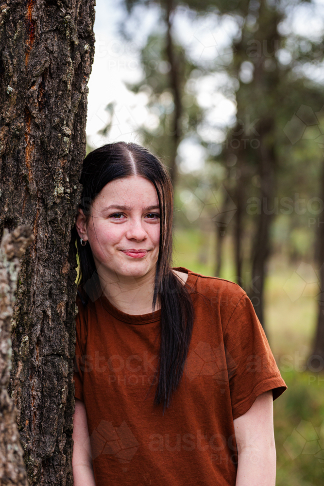 Portrait of teen girl outside leaning against gum tree trunk - Australian Stock Image