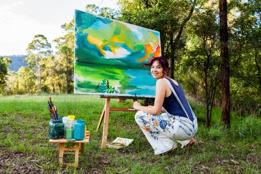 Portrait of teen girl squatting beside art project outdoors - Australian Stock Image