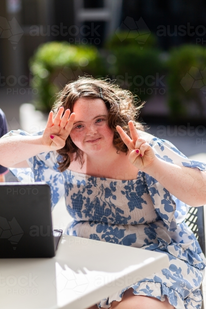 Portrait of teen girl with down syndrome making peace sign - Australian Stock Image