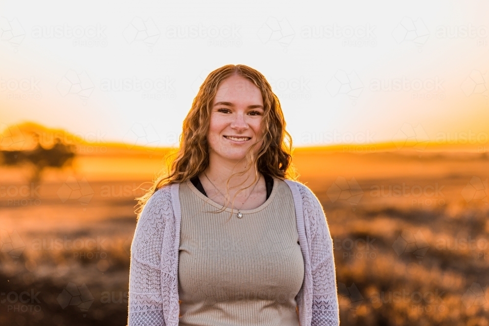 Portrait of teenage girl smiling against sunset rural landscape - Australian Stock Image