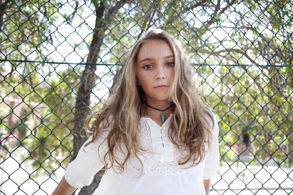 Portrait of teenage girl standing against fence - Australian Stock Image