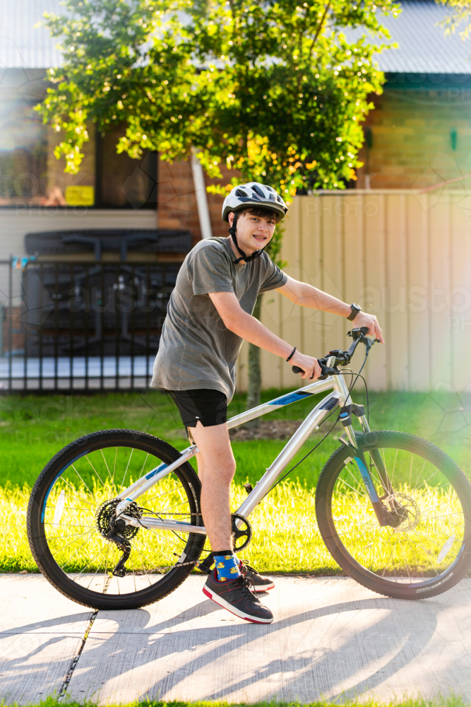portrait of teenaged boy riding bike on footpath wearing helmet for safety - Australian Stock Image