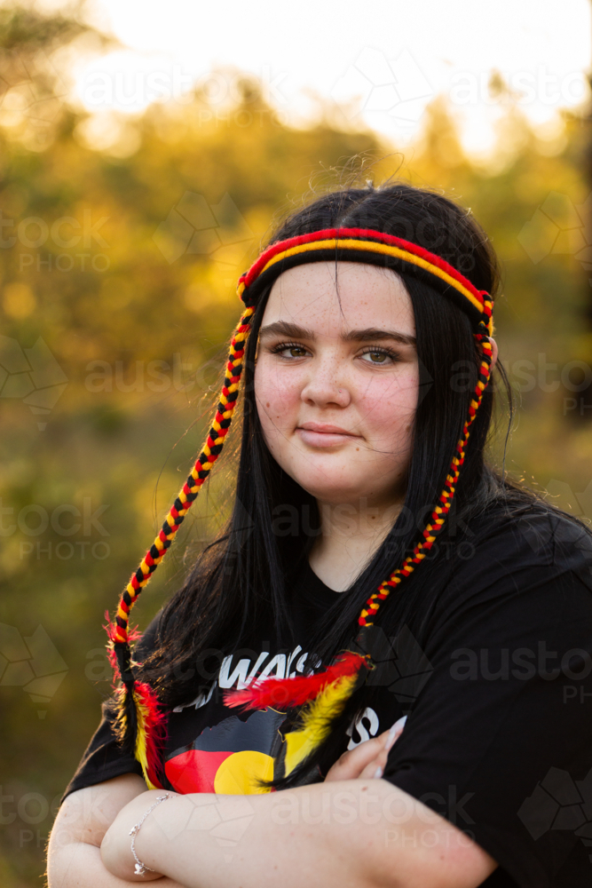 Portrait of thirteen year old aboriginal girl with dark hair and red yellow and black headband - Australian Stock Image