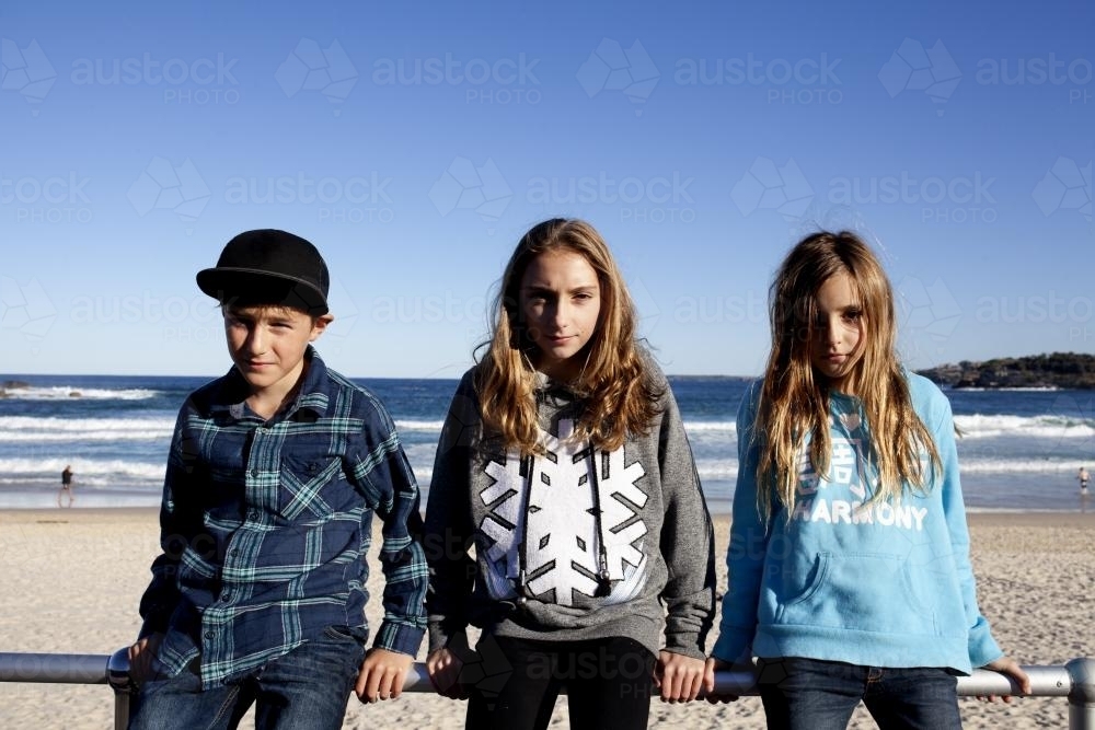 Portrait of three siblings sitting on railing at the beach - Australian Stock Image