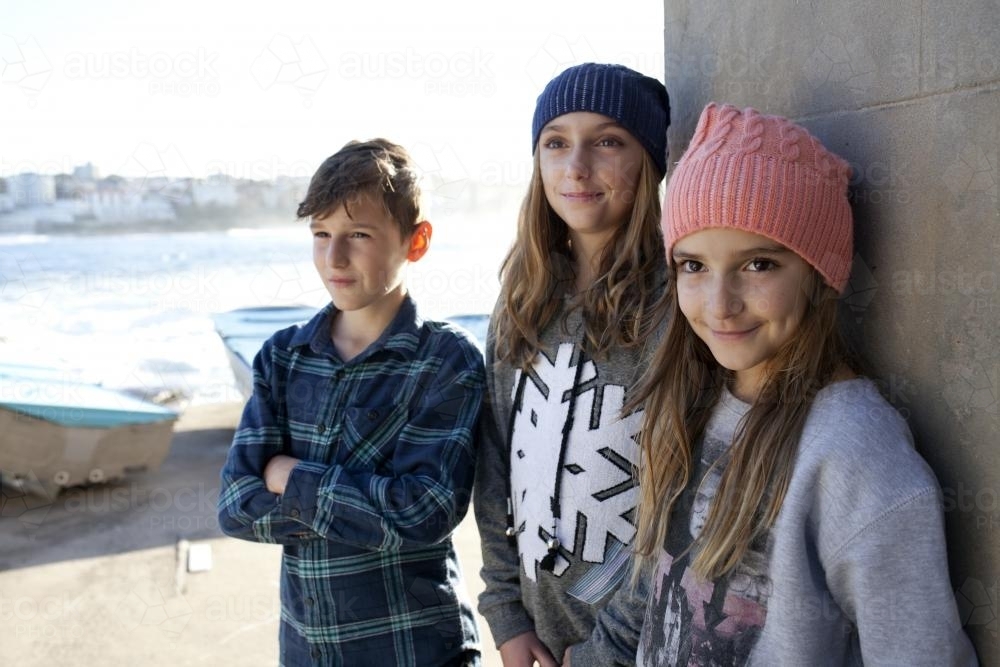 Portrait of three smiling kids  standing against wall by the ocean - Australian Stock Image