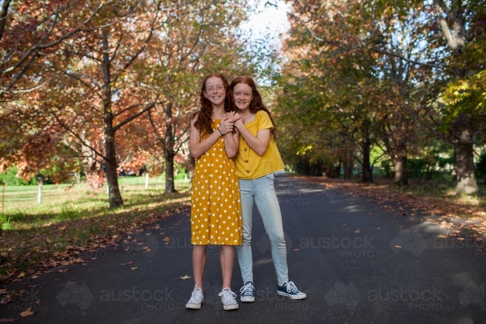 Portrait of two girls in a street lined with Autumn trees : Austockphoto Portrait of two girls in a street lined with Autumn trees - Australian Stock Image