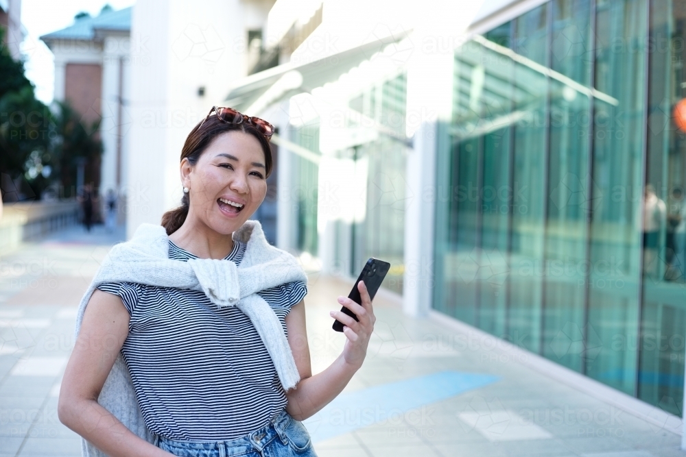 Portrait of woman laughing and holding mobile phone on urban footpath - Australian Stock Image