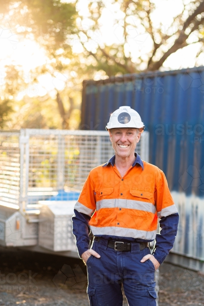 Portrait of worker infront of shipping container with hard hat on - Australian Stock Image