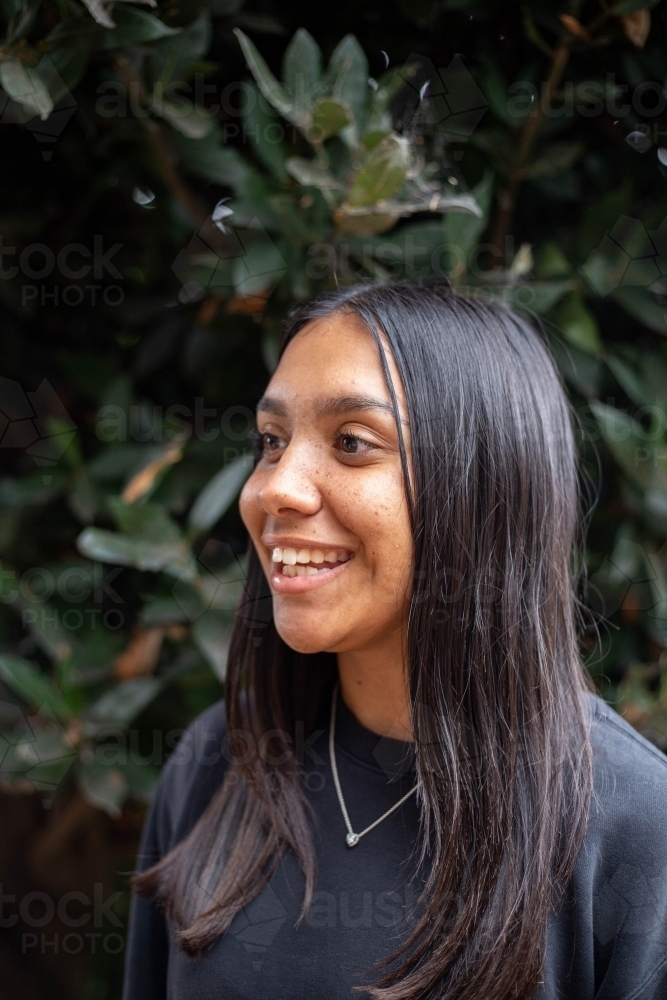 Portrait of young Aboriginal woman in front of foliage - Australian Stock Image