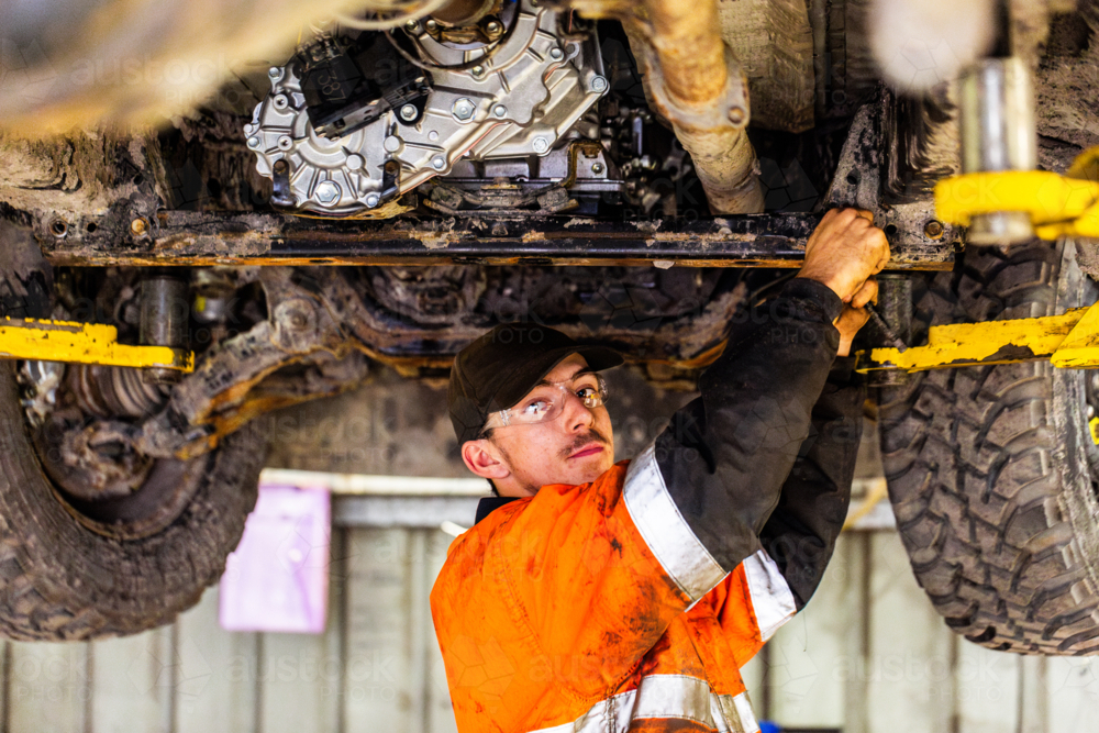 portrait of young aussie mechanic working on repairs under vehicle in workshop - Australian Stock Image