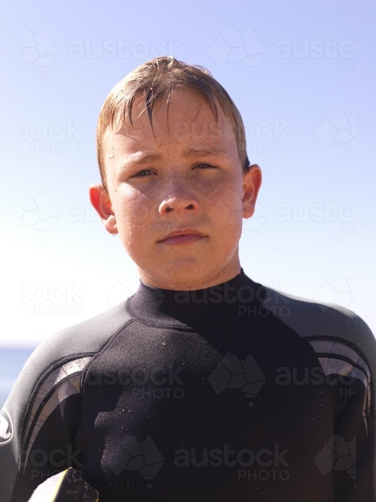 Portrait of young boy coming out of the beach in wetsuit - Australian Stock Image
