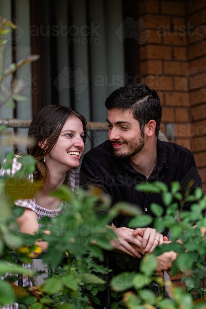 Portrait of young couple leaning on front balcony railing of home they own - Australian Stock Image