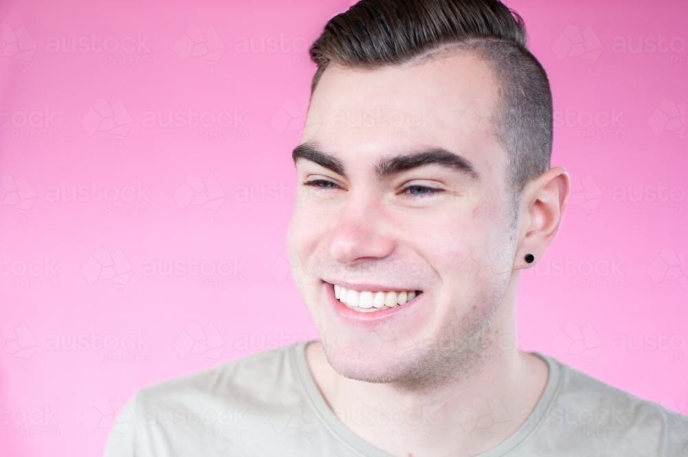 Portrait of young man laughing on plain pink background - Australian Stock Image