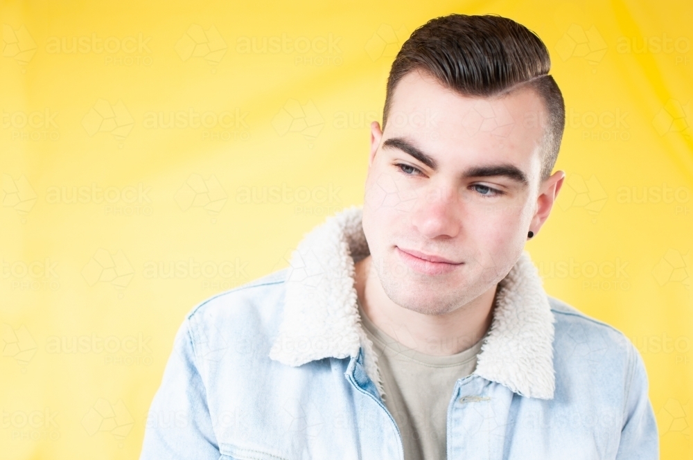 Portrait of young man looking down on plain yellow background - Australian Stock Image