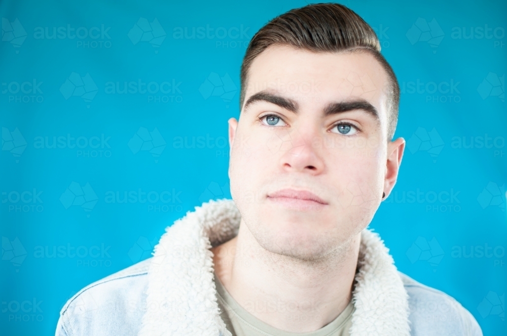 Portrait of young man looking up on plain blue background - Australian Stock Image