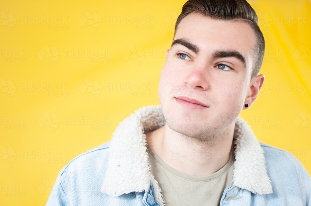 Portrait of young man looking up on plain yellow background - Australian Stock Image