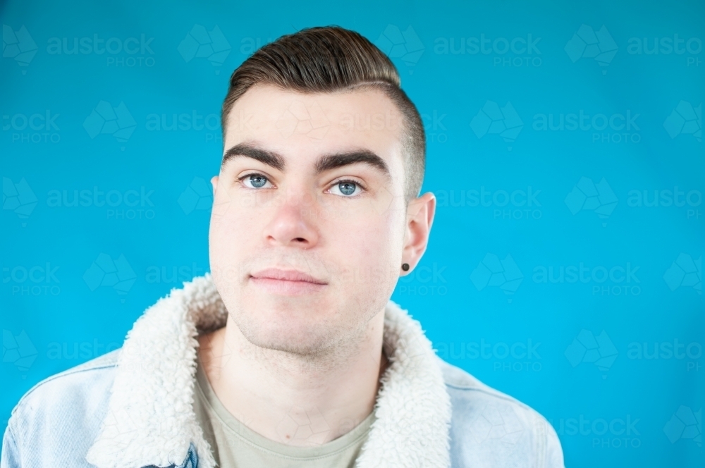 Portrait of young man on plain blue background - Australian Stock Image