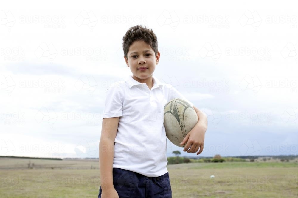 Portrait of young mixed race boy holding rugby football - Australian Stock Image