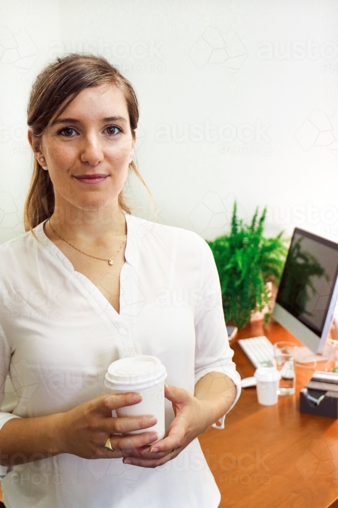Portrait of young professional woman holding a coffee in the office - Australian Stock Image