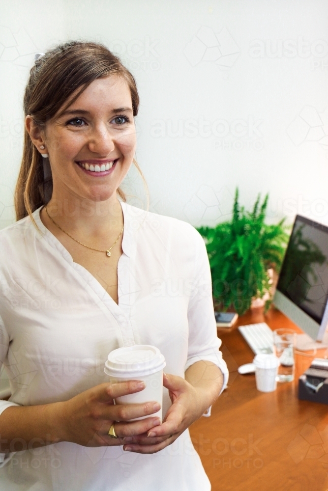 Portrait of young professional woman smiling holding a coffee in the office - Australian Stock Image