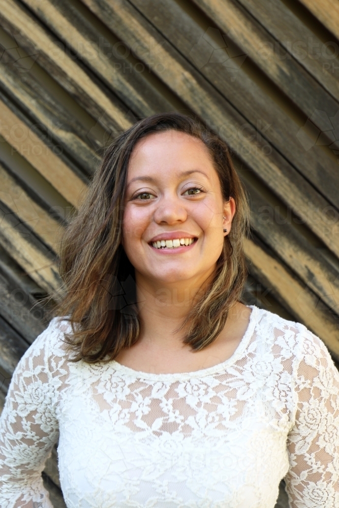 Portrait of young woman smiling in front of textured wooden panelling - Australian Stock Image