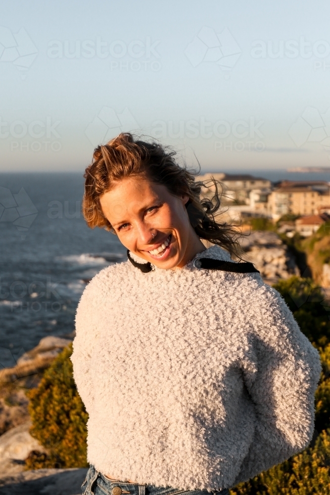 Portrait of young woman smiling on coastal clifftop at sunrise - Australian Stock Image