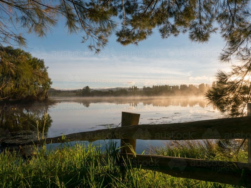 Post and rail fence overlooking a dam with mist rising - Australian Stock Image