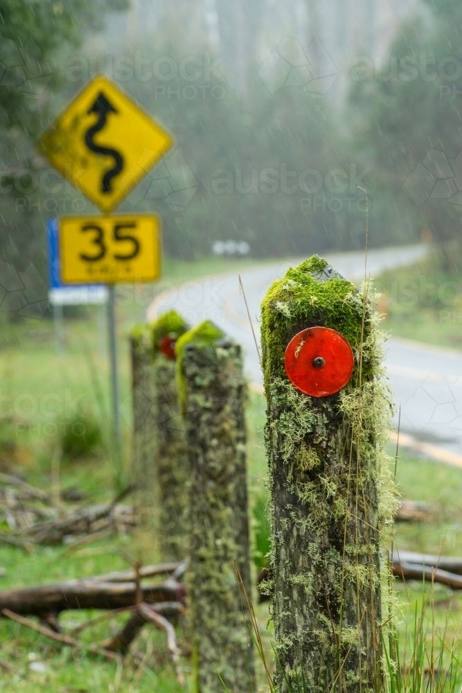 Posts on a roadside covered in moss and a road sign in the rain - Australian Stock Image
