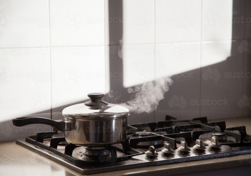 Pot boiling on kitchen stove - Australian Stock Image