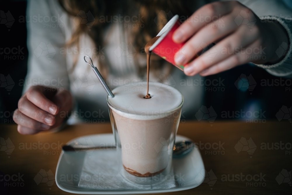 Pouring melted chocolate into a hot chocolate - Australian Stock Image