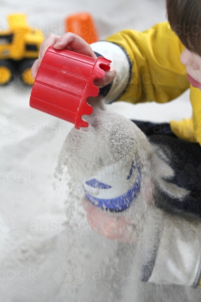 pouring sand between cups in sandpit - Australian Stock Image