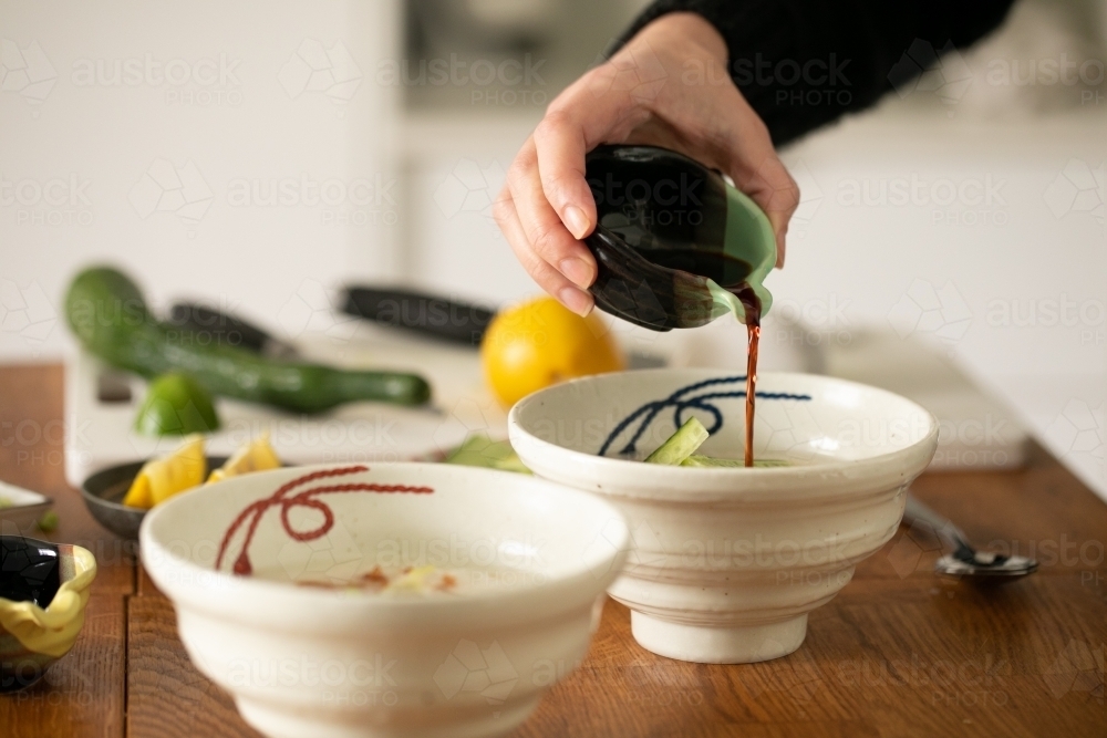 Pouring soy sauce into a bowl of congee - Australian Stock Image