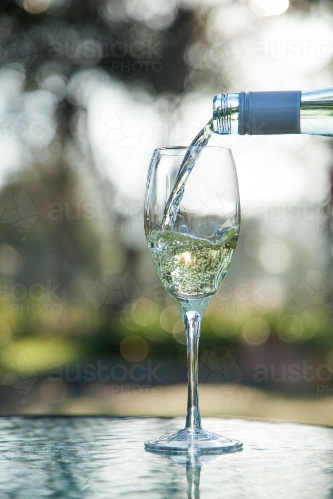 Pouring white wine from bottle into a glass on table outside - Australian Stock Image