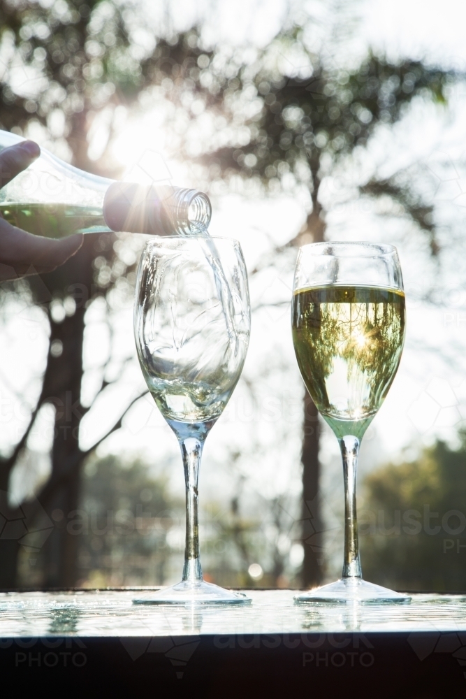 Pouring white wine from bottle into glasses on table outside - Australian Stock Image