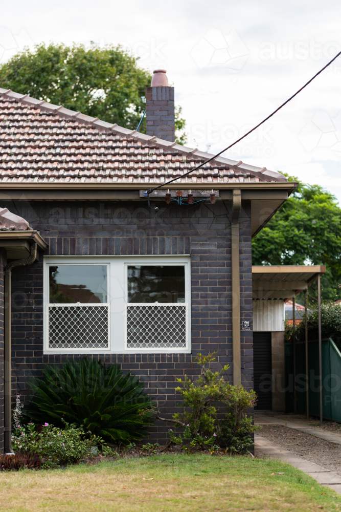 Power connection point to house with tiled roof and driveway to empty carport - Australian Stock Image