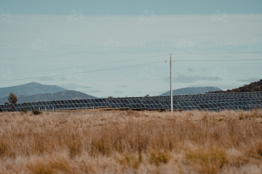 Power lines in front of solar farm panels for renewable energy with mountains in the background. - Australian Stock Image