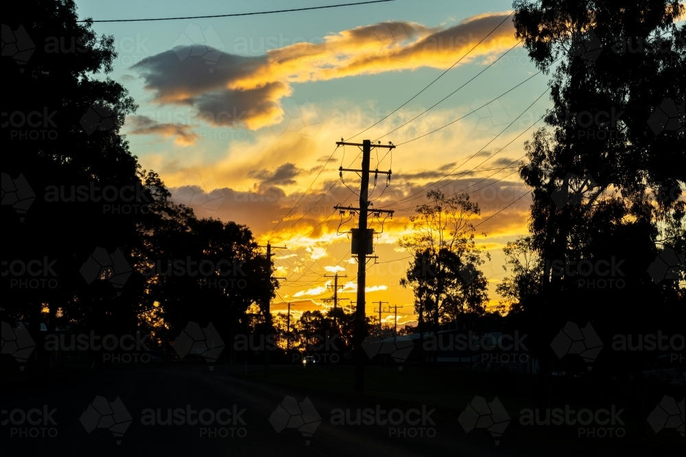 Power pole with electricity wires silhouetted against sunset clouds in sky - Australian Stock Image
