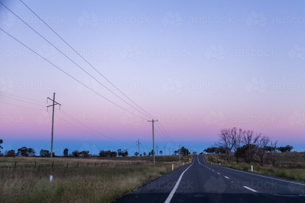 Power poles and lines beside country road at dusk - Australian Stock Image