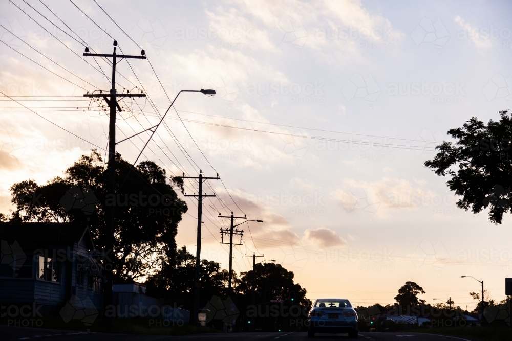Power poles and lines silhouetted along street at sunset - Australian Stock Image