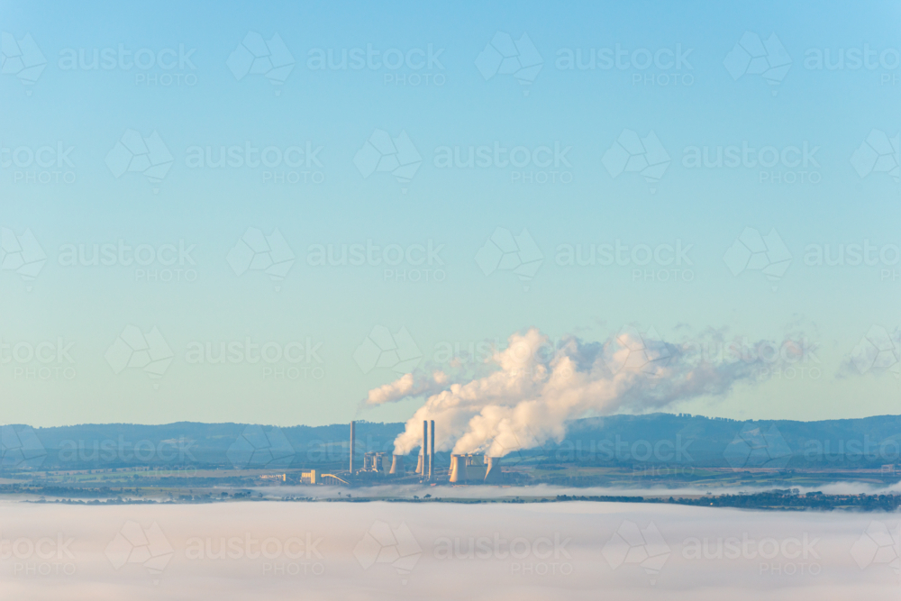 Power station chimneys emitting steam above low morning fog in rural landscape. - Australian Stock Image