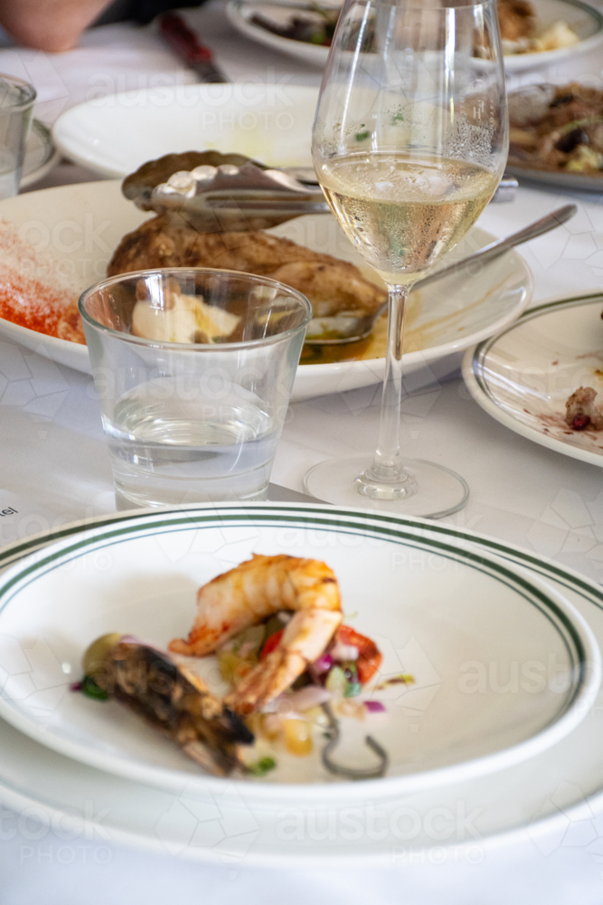 Prawn on a plate on a dinner table with glass of wine vertical - Australian Stock Image