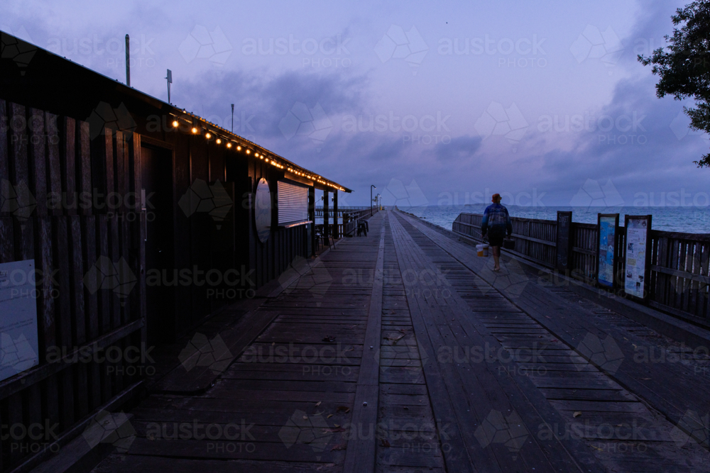 pre-dawn jetty with festoon lights and someone walking out to fish - Australian Stock Image
