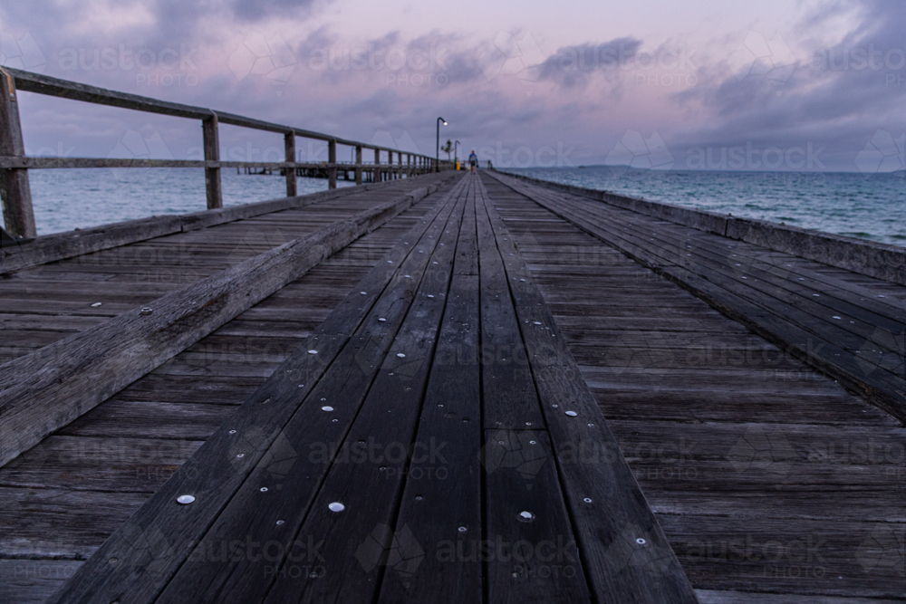 pre-dawn on an old timber jetty with someone going fishing in the distance - Australian Stock Image