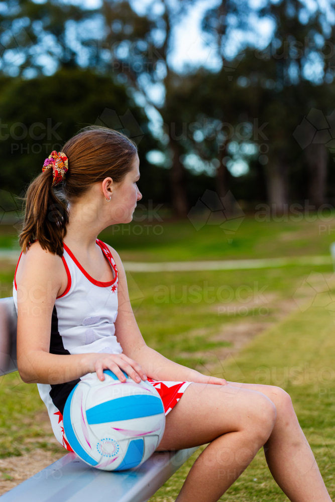 Pre-teen aboriginal girl sitting on sideline bench with netball ball - Australian Stock Image