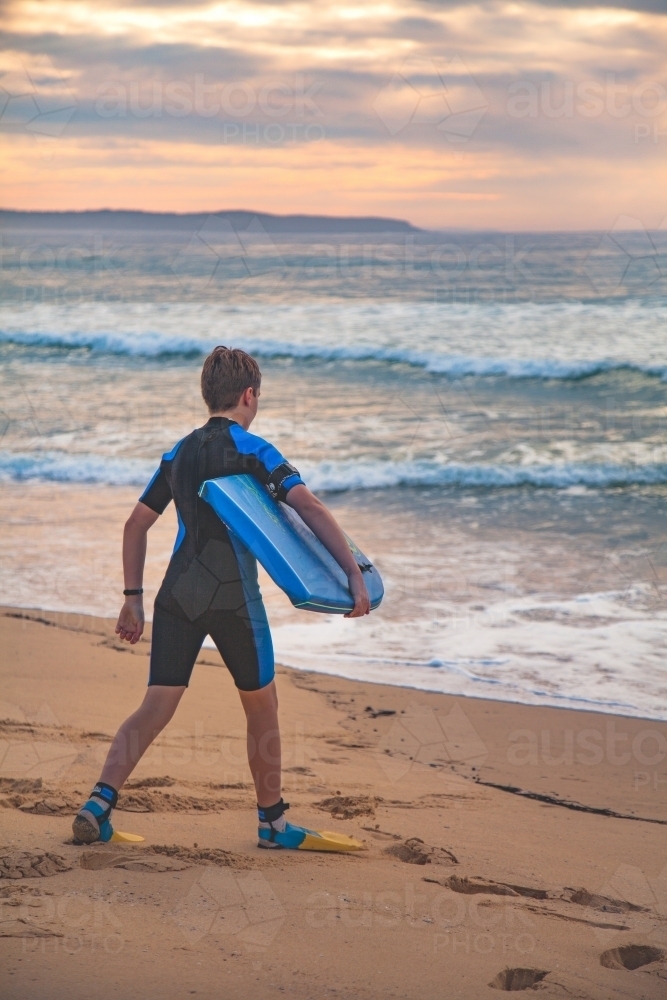 Pre-teen boy preparing to go body boarding at beach - Australian Stock Image