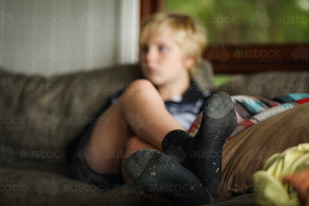 Pre-teen boy relaxing on couch with focus on dirty socks - Australian Stock Image