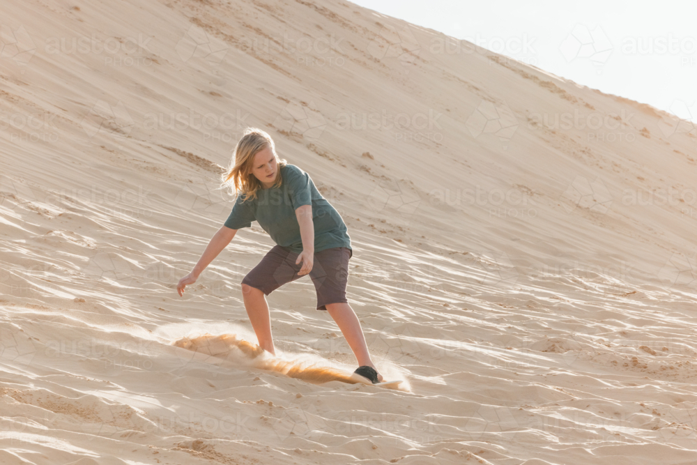 Pre-teen boy riding board down sand dune at Birubi Beach, Port Stephens - Australian Stock Image